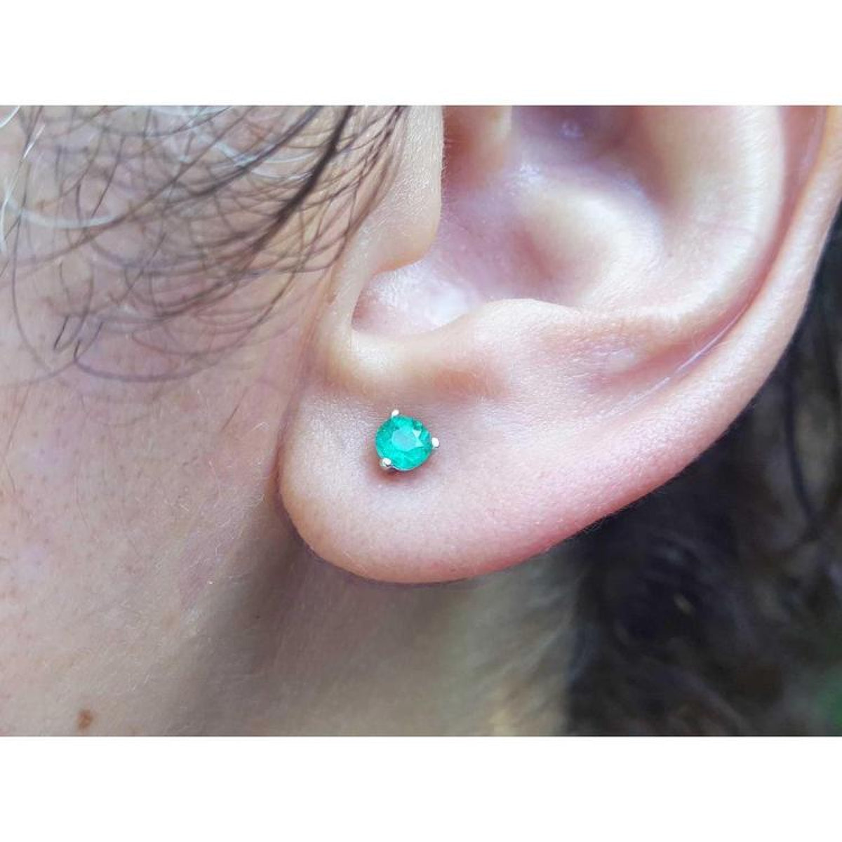 An earlobe wearing a martini emerald stud earring in white gold.