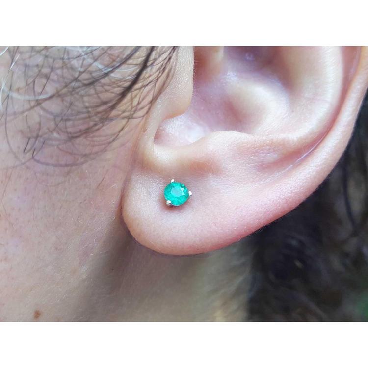 An earlobe wearing a martini emerald stud earring in white gold.