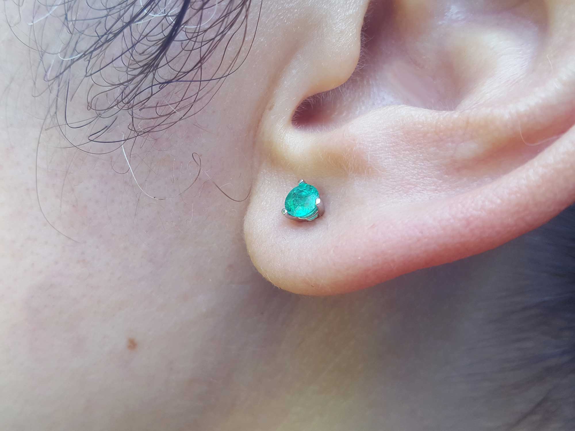 A woman&#39;s ear wearing a three pong set martini emerald stud earrings.