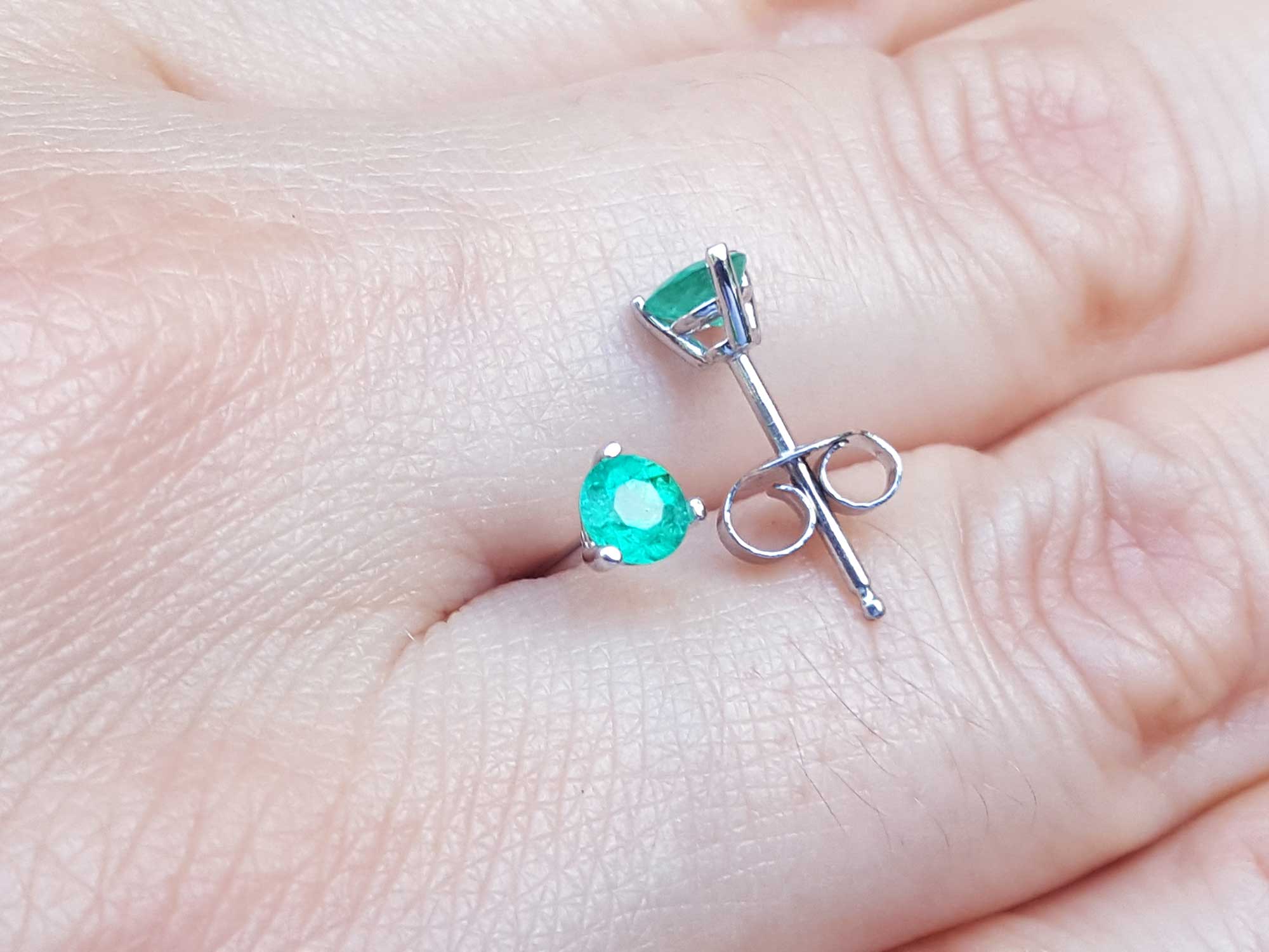 Displaying on a hand a pair of push backs martini emerald stud earrings.