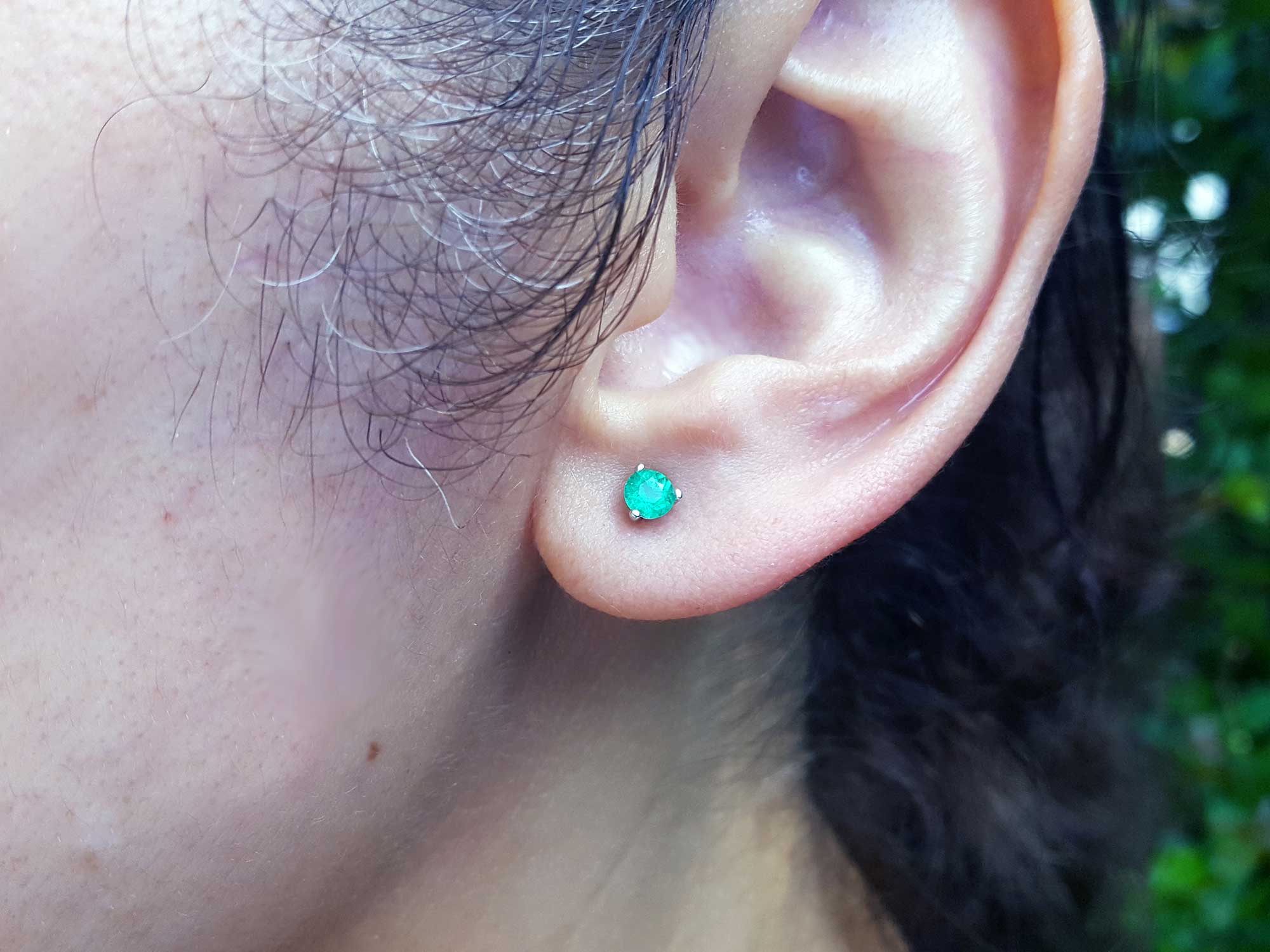 Real emerald stud earrings martini style on a woman&#39;s ear.