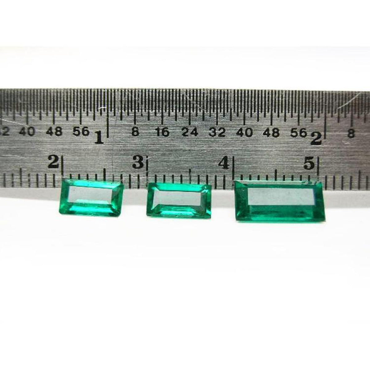 Three baguette-cut natural loose Colombian emeralds, deep bluish-green, displayed with a ruler for scale.