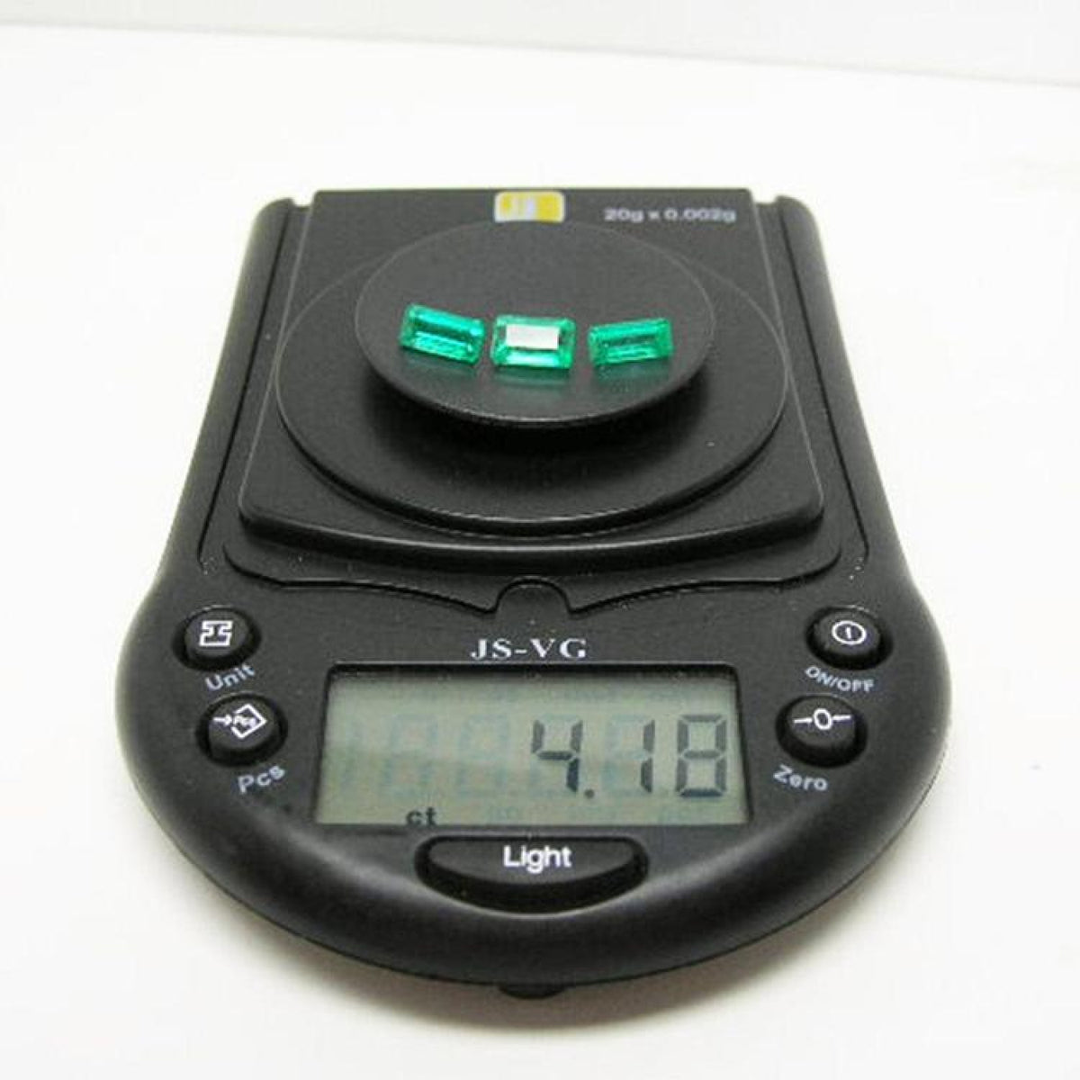 Three emerald-cut natural Colombian emeralds, 4.18 carats, on a black digital jewelry scale.