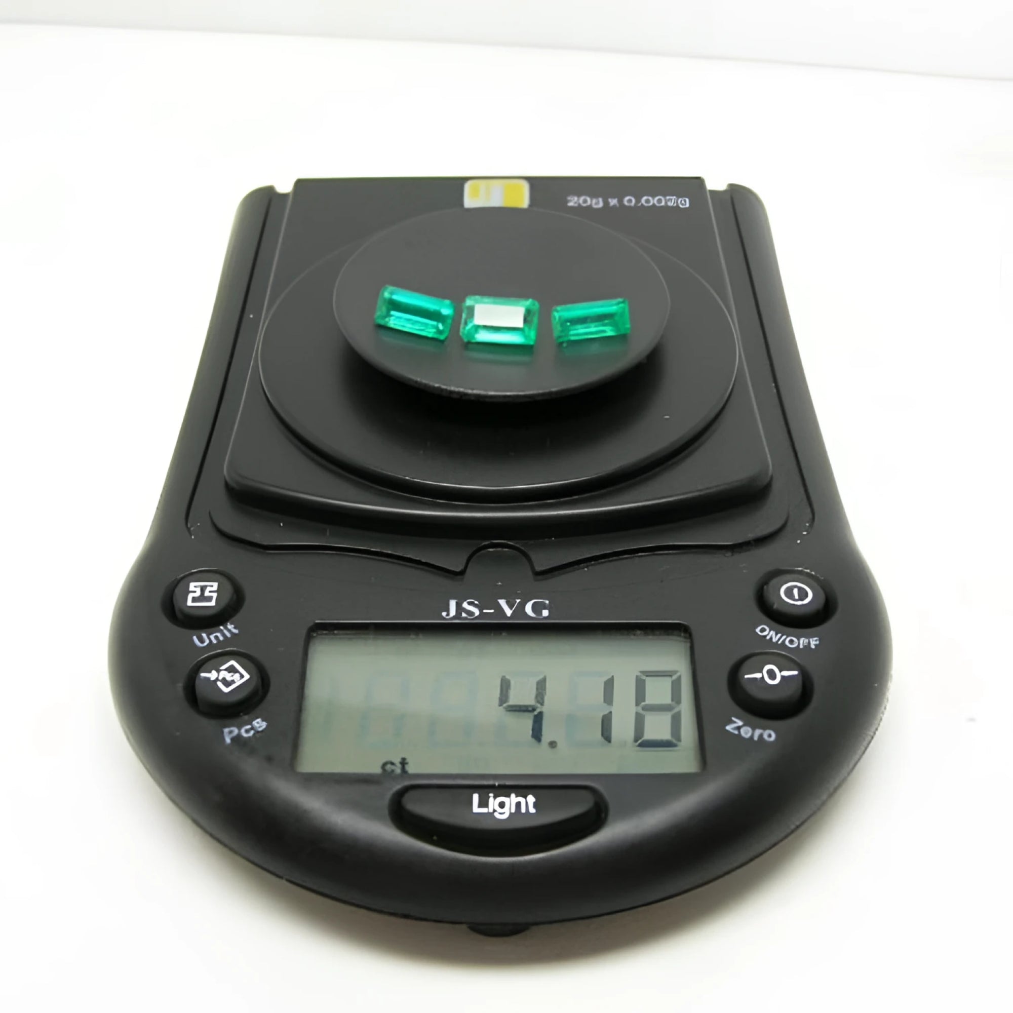 Three emerald-cut natural Colombian emeralds, 4.18 carats, on a black digital jewelry scale.