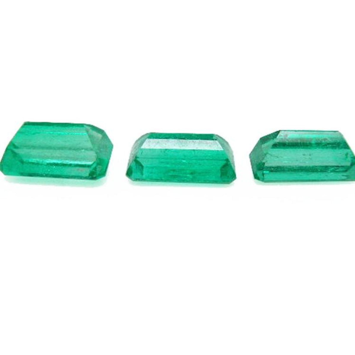 Three emerald-cut natural Colombian emeralds, a matched set for earrings and pendant, on a white background.