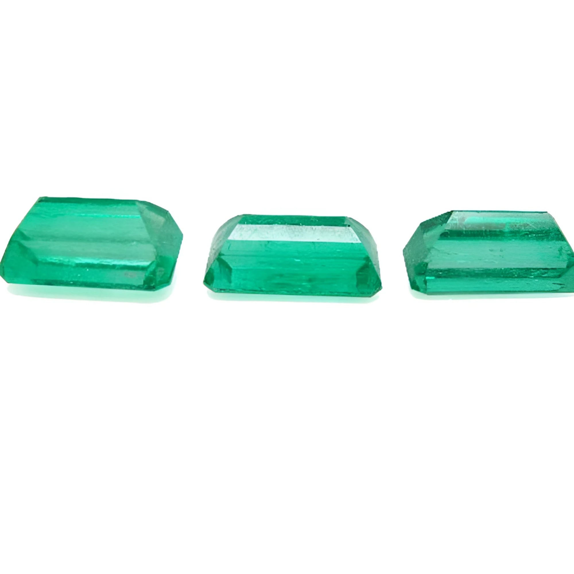 Three emerald-cut natural Colombian emeralds, a matched set for earrings and pendant, on a white background.