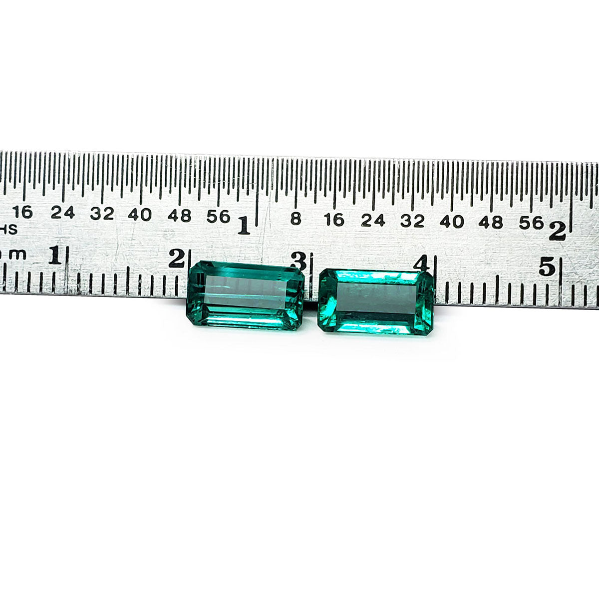 Emerald-cut matching pair loose emeralds from Muzo Colombia, front side tables and crowns visible with a ruler sizer