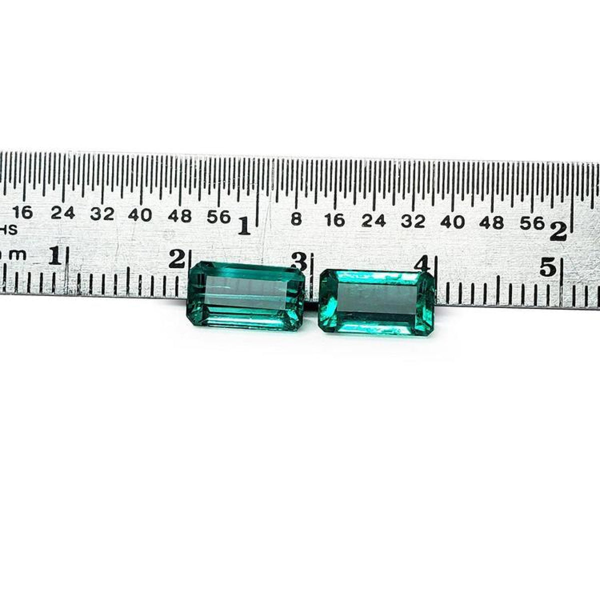 Emerald-cut 3.38 ct. matching pair loose emeralds with vibrant bluish-green color, displayed next to a ruler.