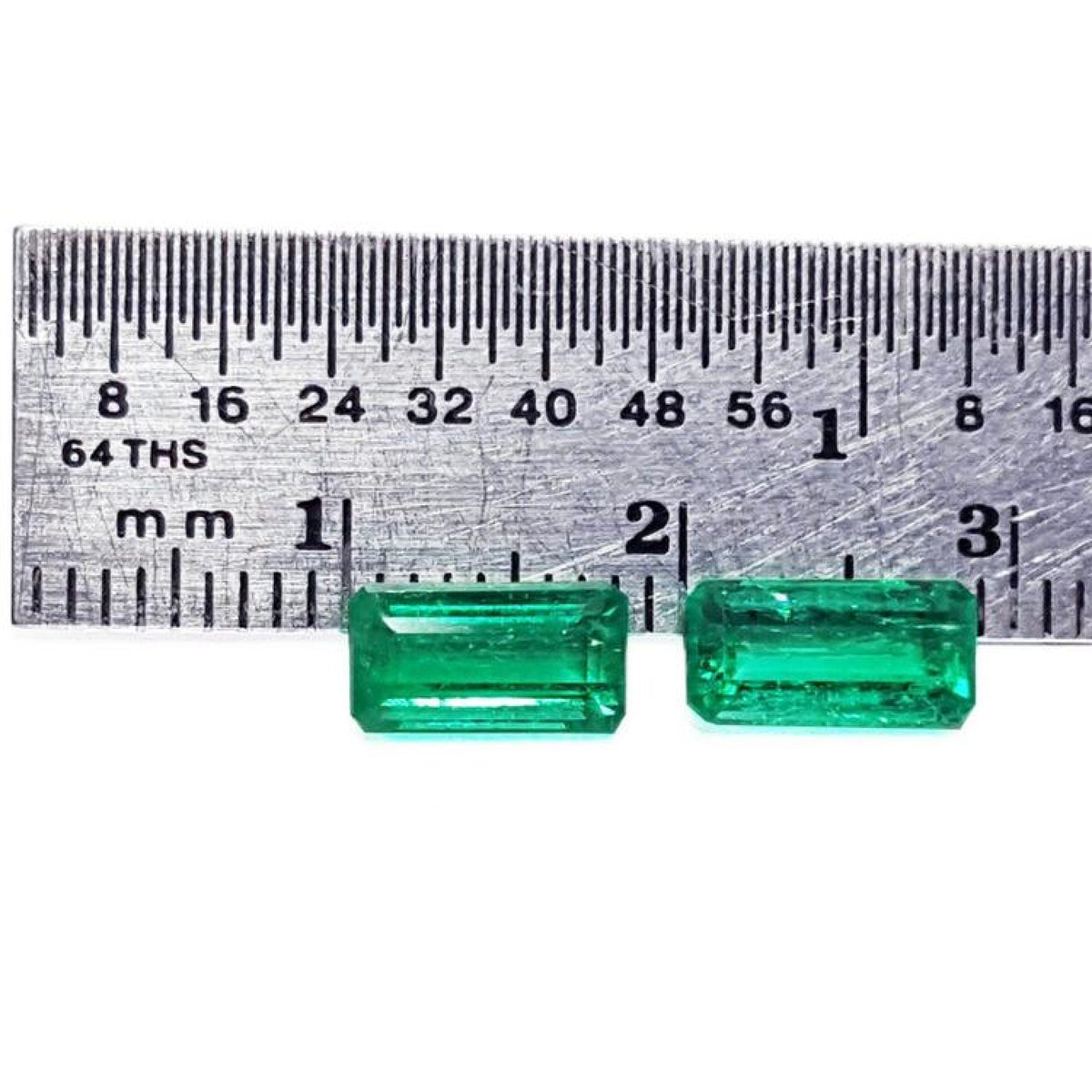 Matched pair of natural emerald-cut green emeralds next to a ruler for scale.