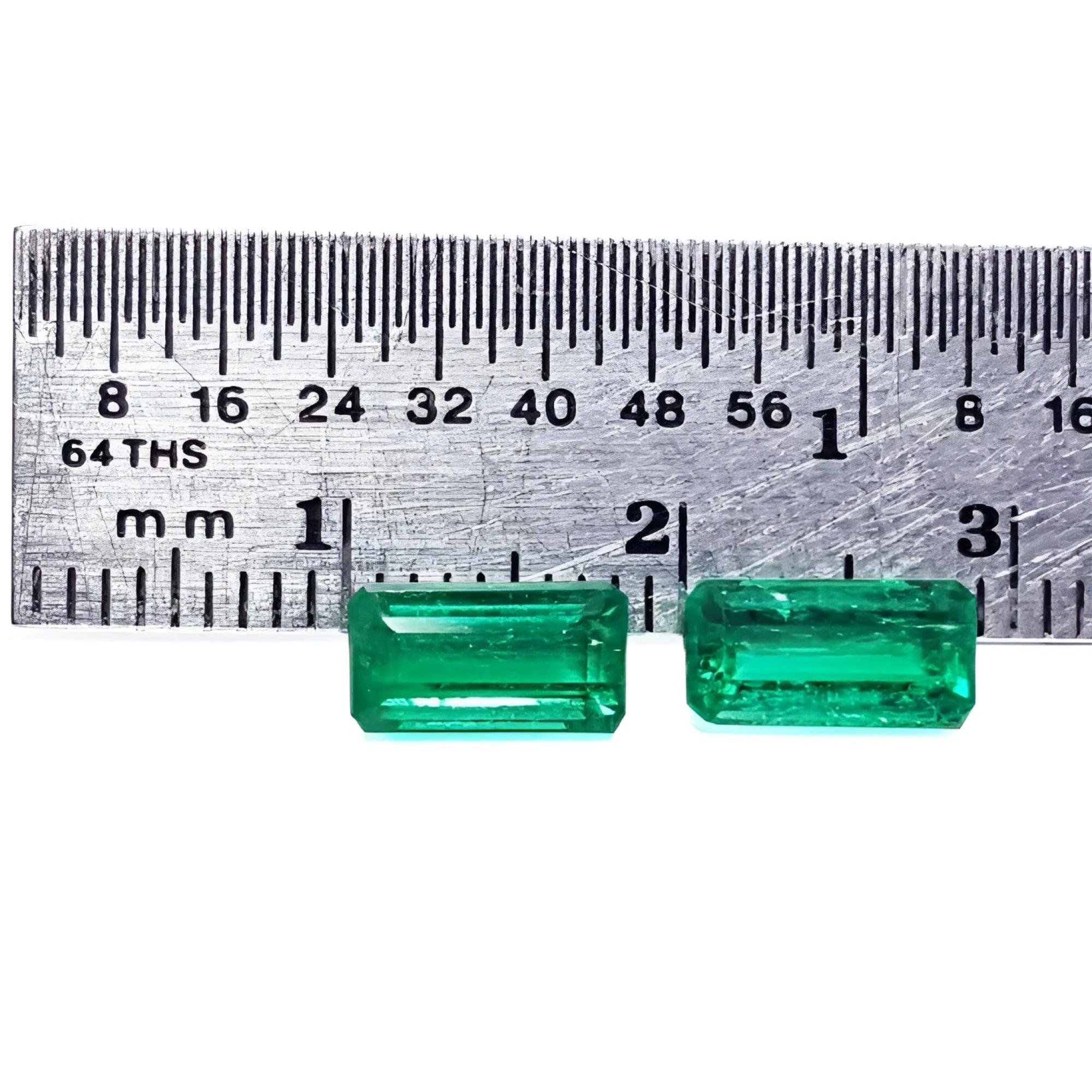 Matched pair of natural emerald-cut green emeralds next to a ruler for scale.
