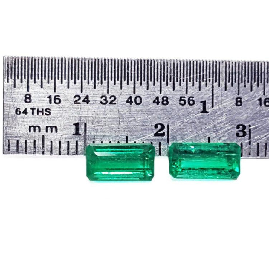 Matched pair of natural emerald-cut green emeralds next to a ruler for scale.