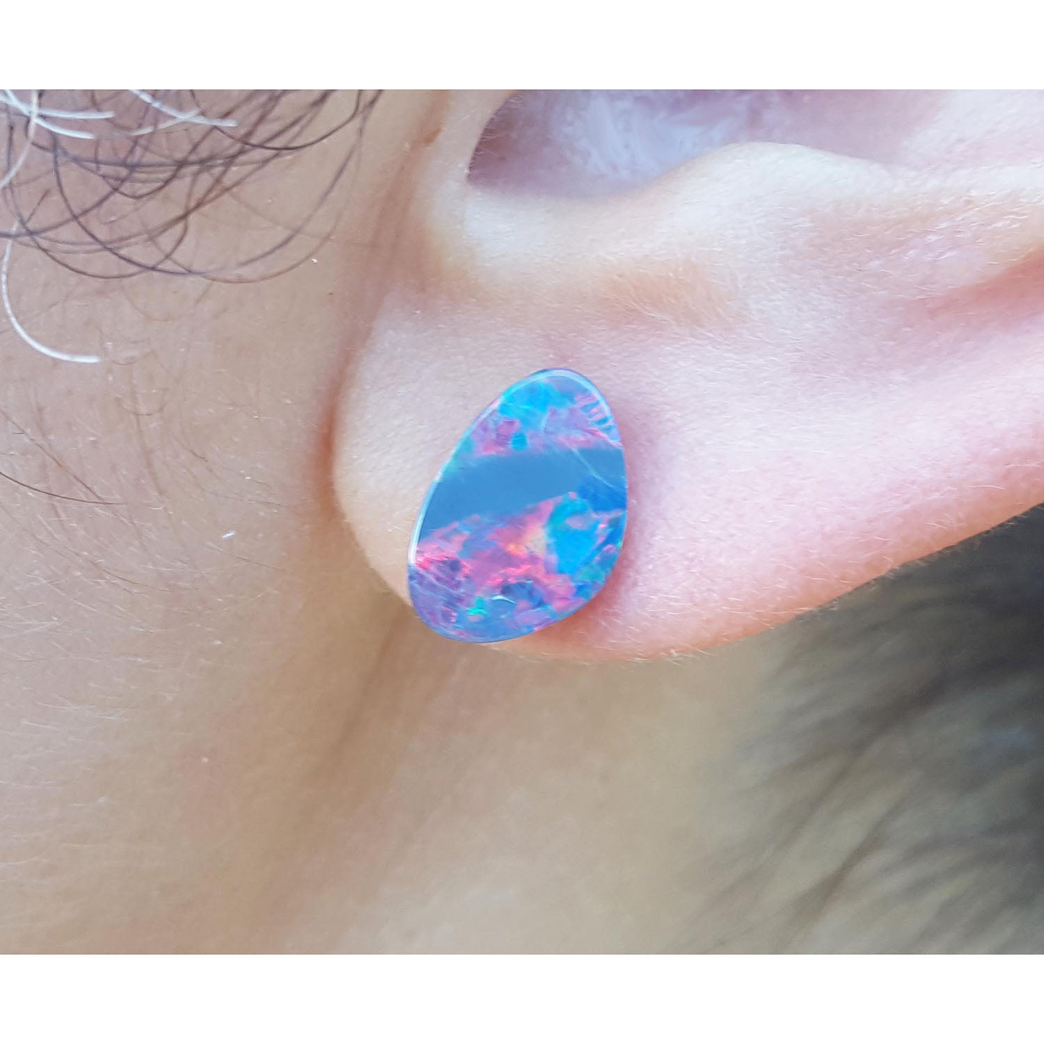 Close-up of a colorful teardrop-shaped Australian opal earring worn on an ear.