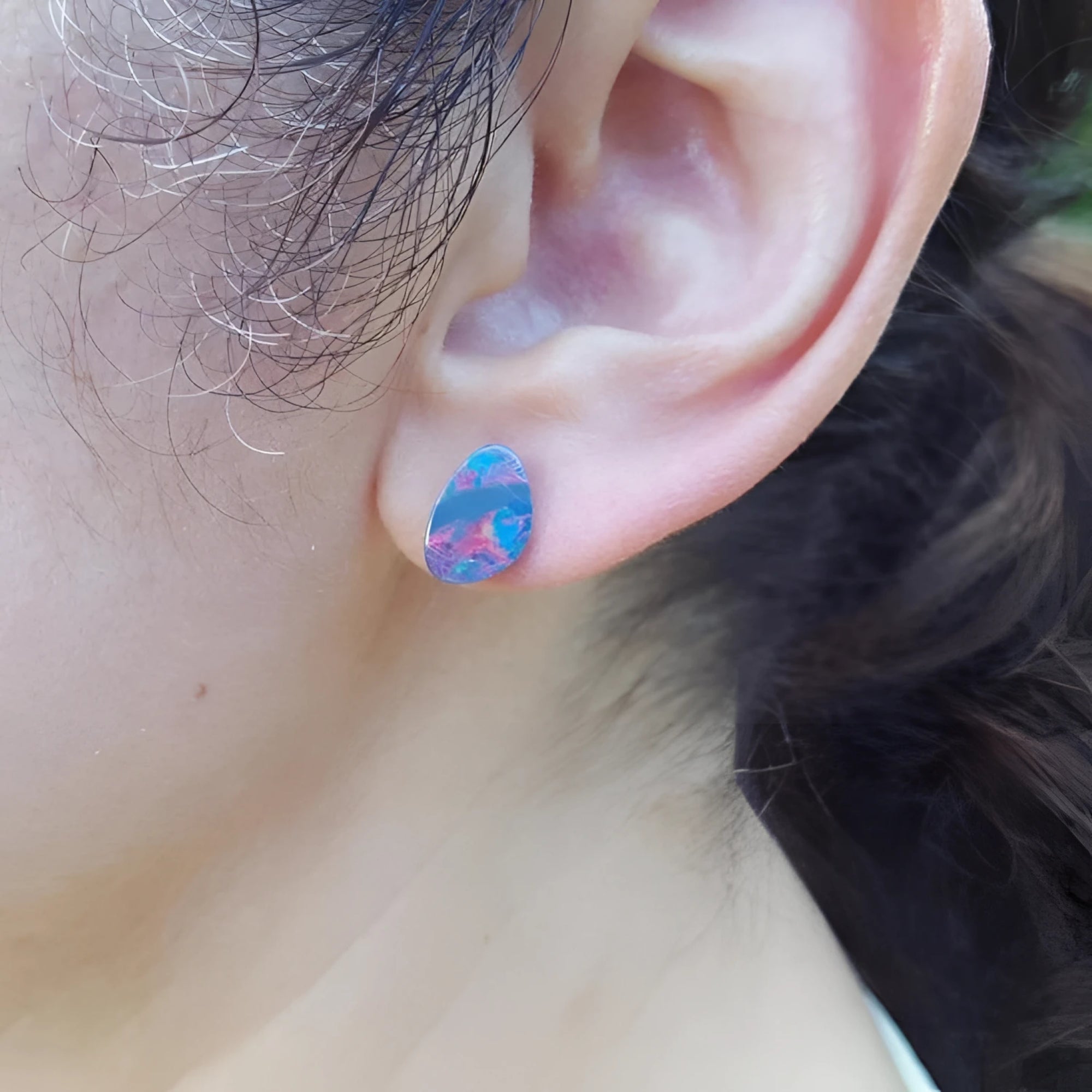 Teardrop Australian doublet opal earring with incandescent red, blue, and green flashes on an ear.