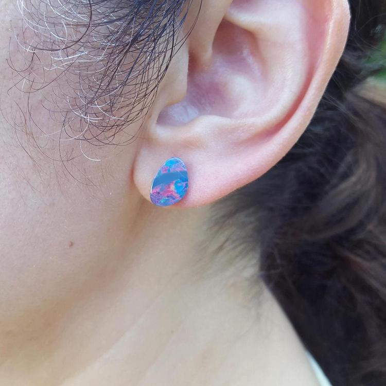 Close-up of an ear wearing a colorful Australian opal stud earring.
