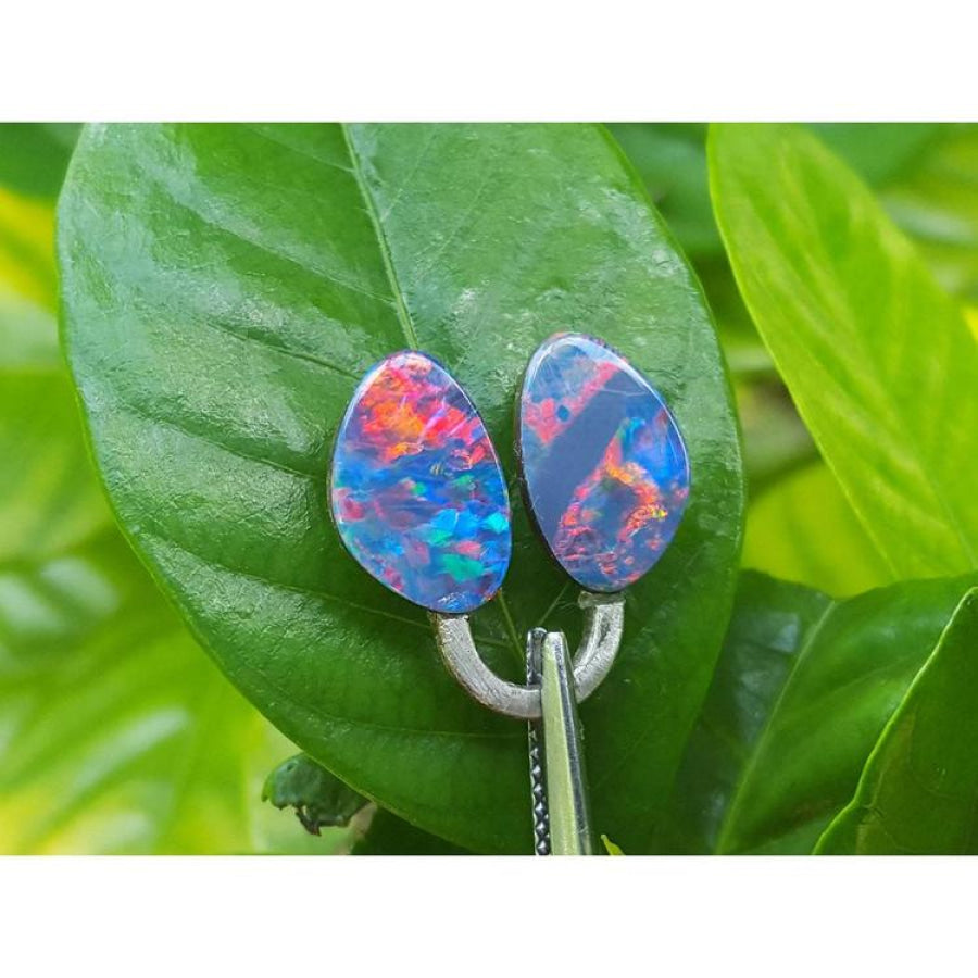 Matching pair of 4.72 ct Australian doublet opals with red, blue, and green flashes on a green leaf.