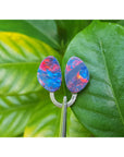 Opal earrings on a green leaf with a blurred plant background.
