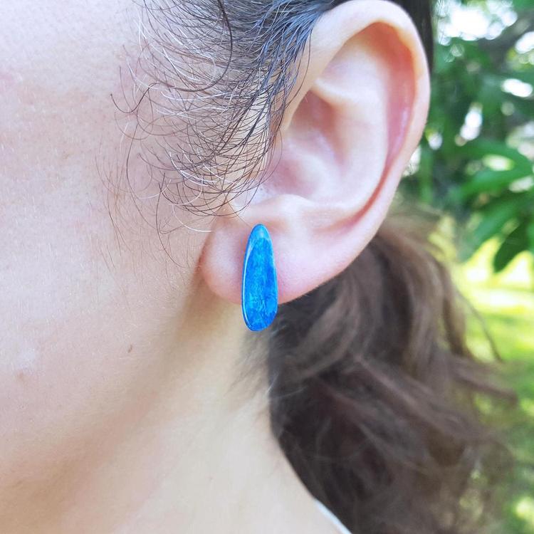 Close-up of an ear wearing a blue opal earring with a blurred green background.
