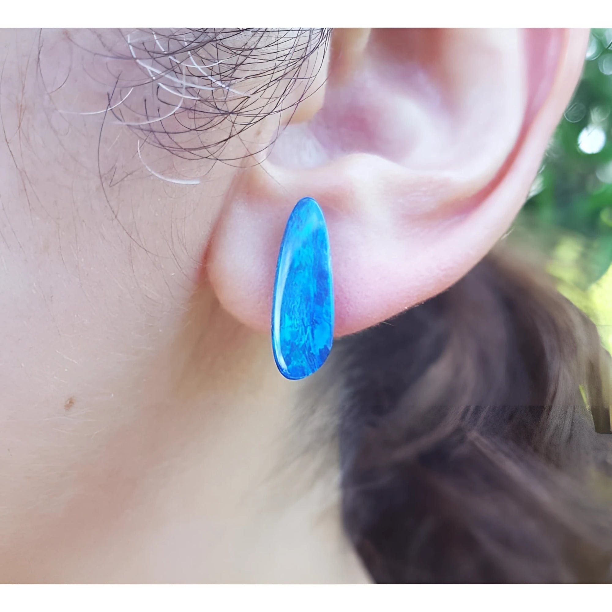 Deep blue Australian doublet opal earring with green flashes, worn on an ear.
