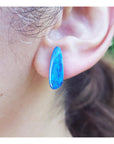 Close-up of an ear wearing a blue opal earring with blurred background