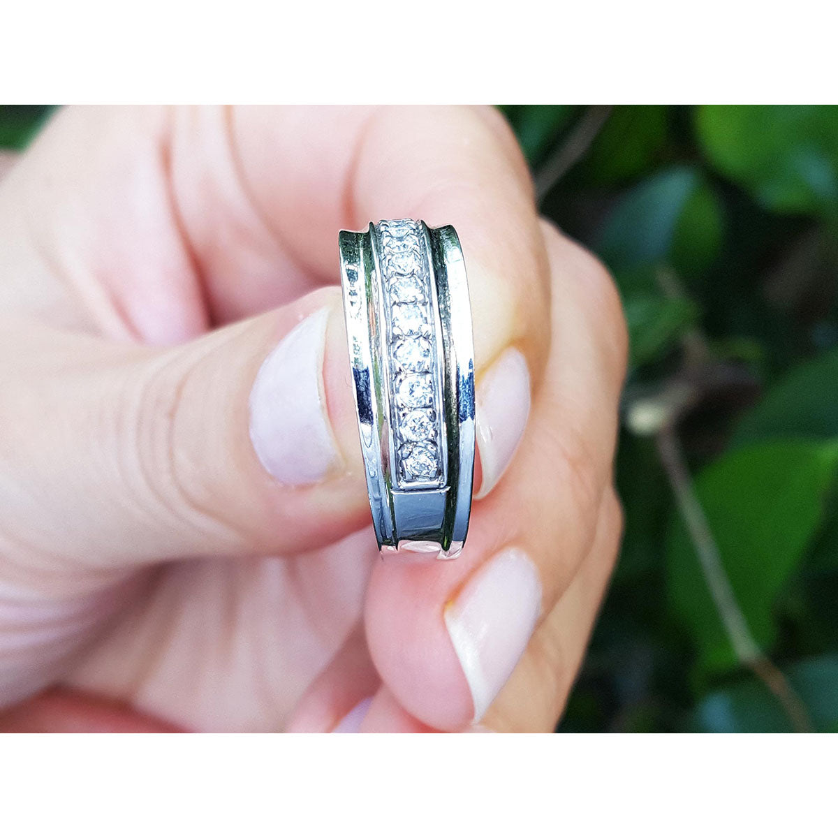 Natural diamond band ring for men in 14K white gold, held between fingers against a blurred green background.