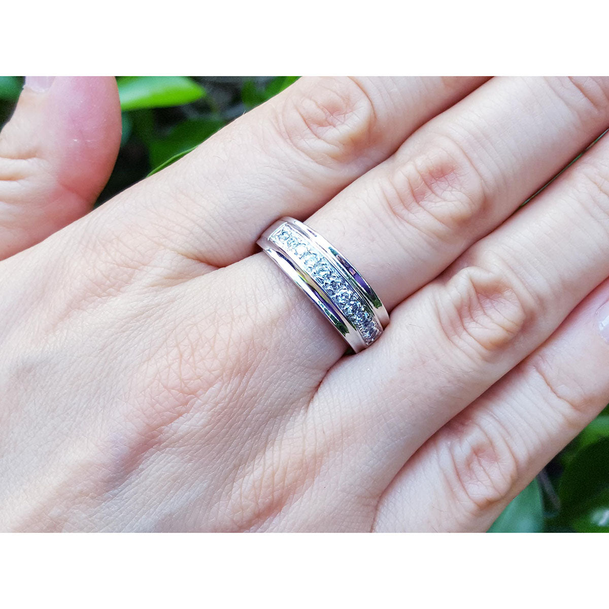 Natural diamond band ring for men in 14K white gold, on a person&#39;s finger against a blurred green background