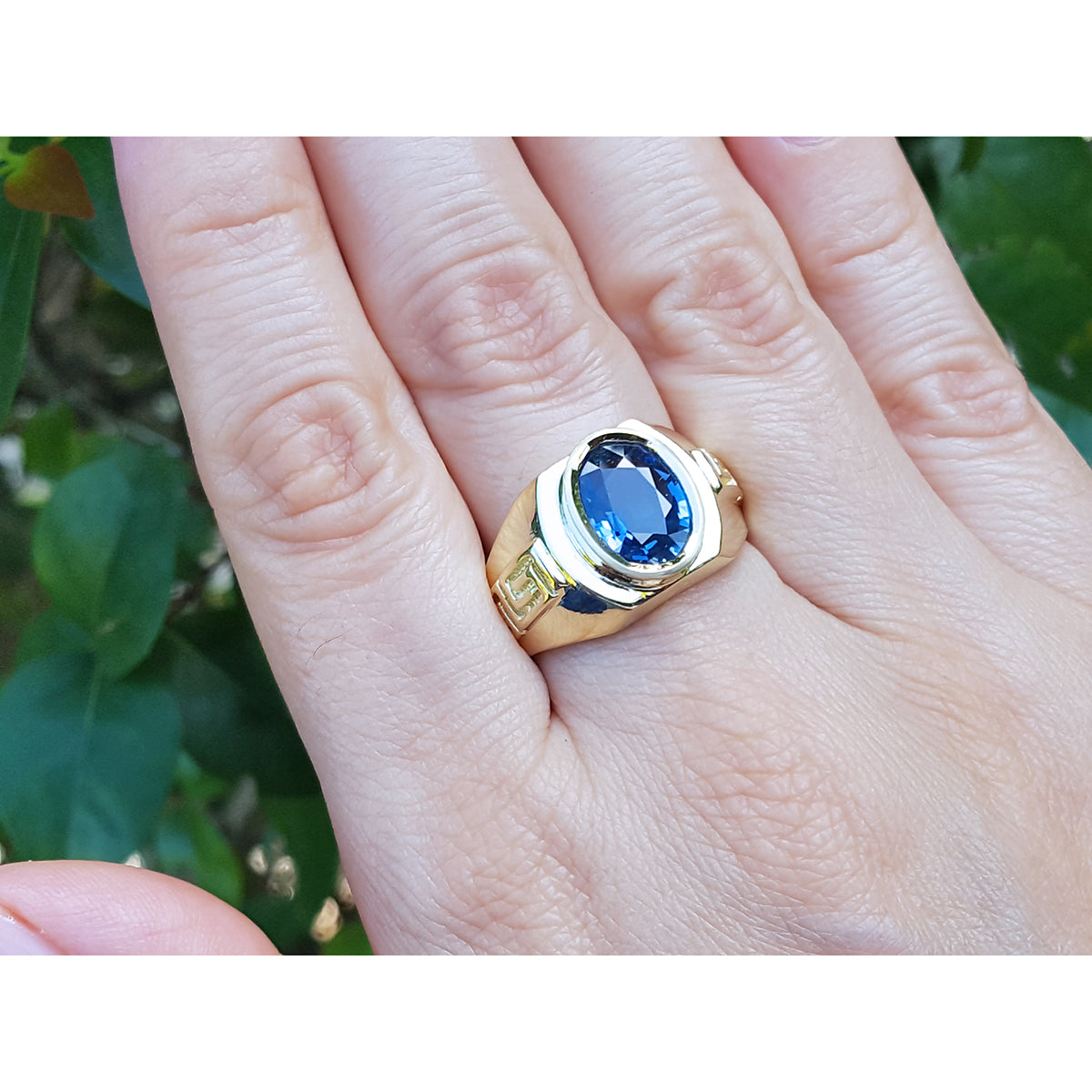 Gold ring with a blue oval cut sapphire gemstone on a hand against a natural background