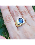 Gold ring with a blue oval cut sapphire gemstone on a hand against a natural background