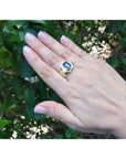 Hand wearing a gold blue sapphire ring against a green leafy background