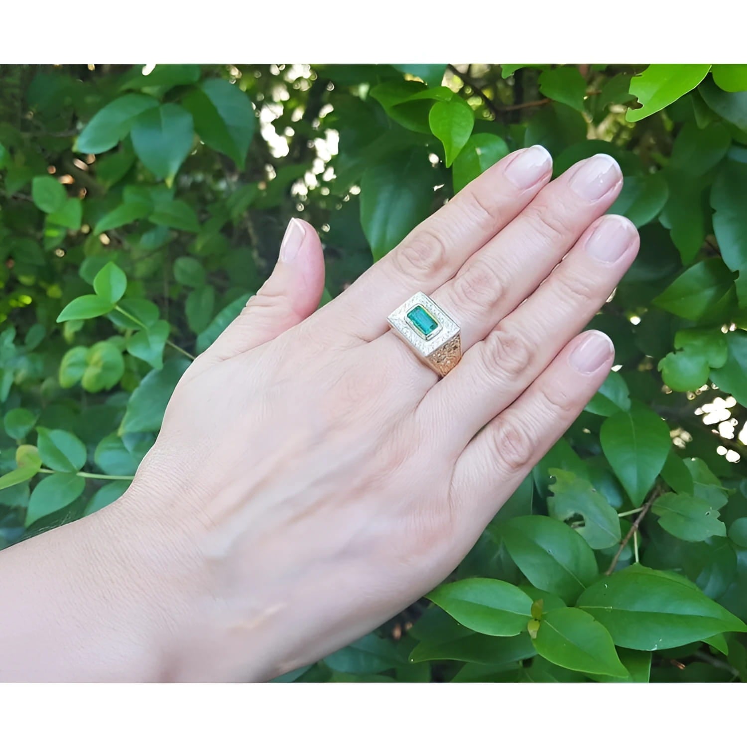 Men's 14K yellow gold ring with a bezel-set emerald gemstone framed by diamonds, worn on a hand.