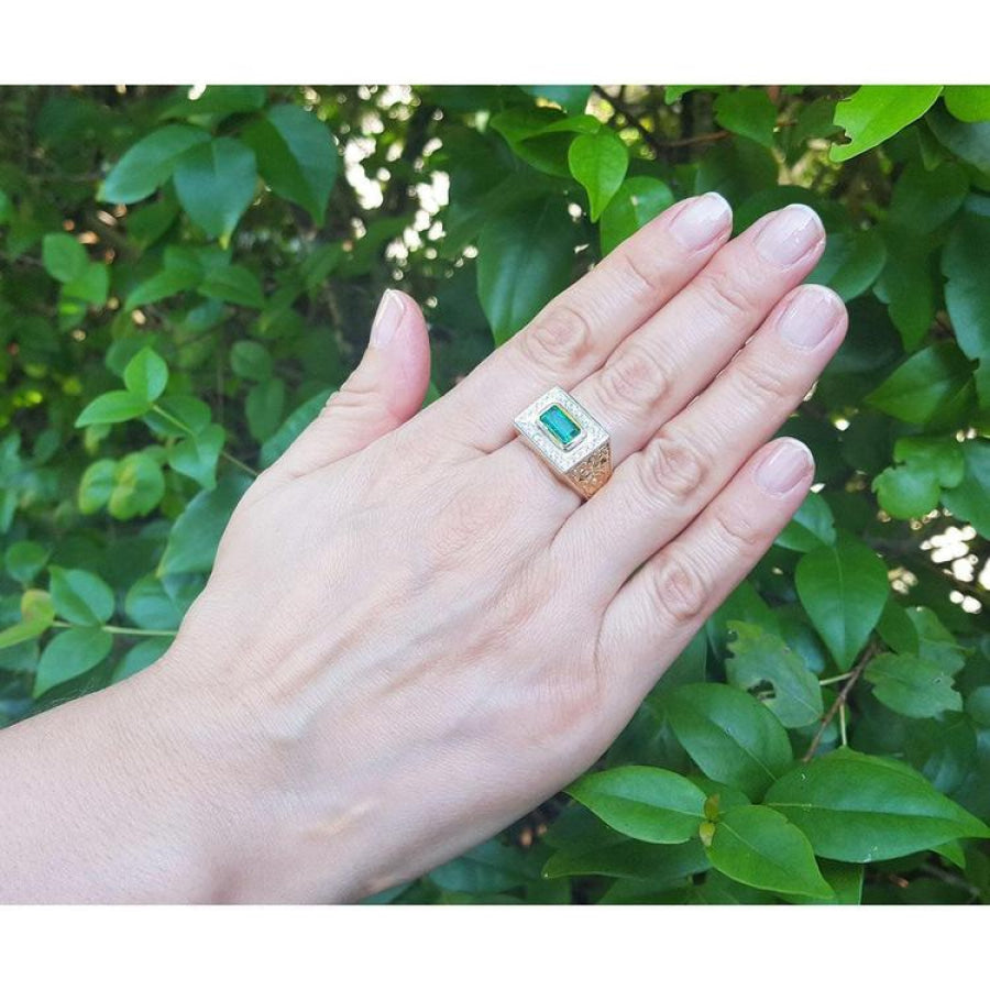 Men's 14K yellow gold ring with a bezel-set emerald gemstone framed by diamonds, worn on a hand.