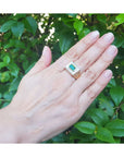Hand wearing a ring for men with a genuine emerald against a leafy background.