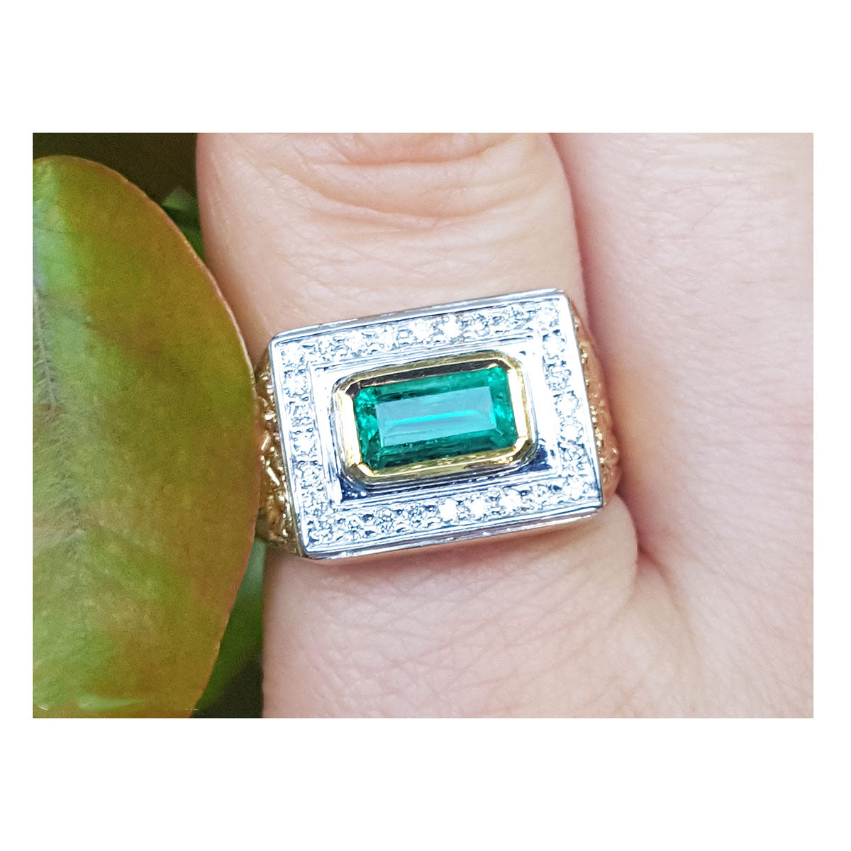 Gold mens ring with emerald and diamonds on a finger.