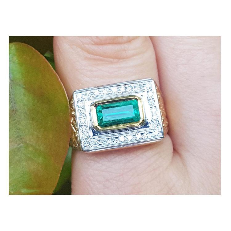 Gold mens ring with emerald and diamonds on a finger.