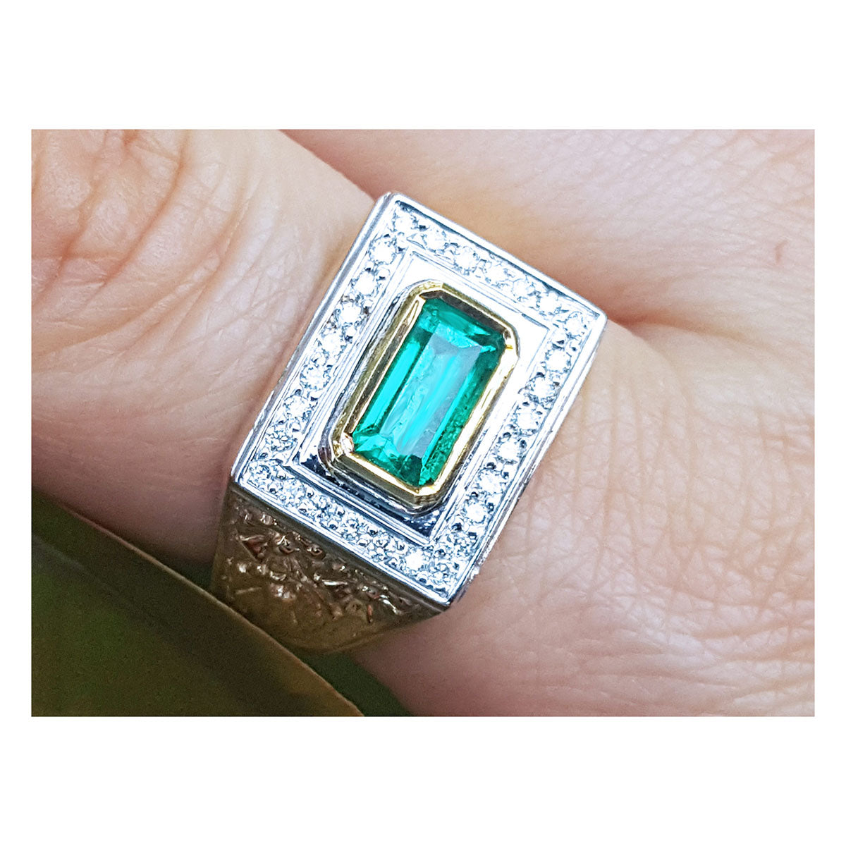 Men&#39;s gold ring with emerald and diamond accents on a finger.