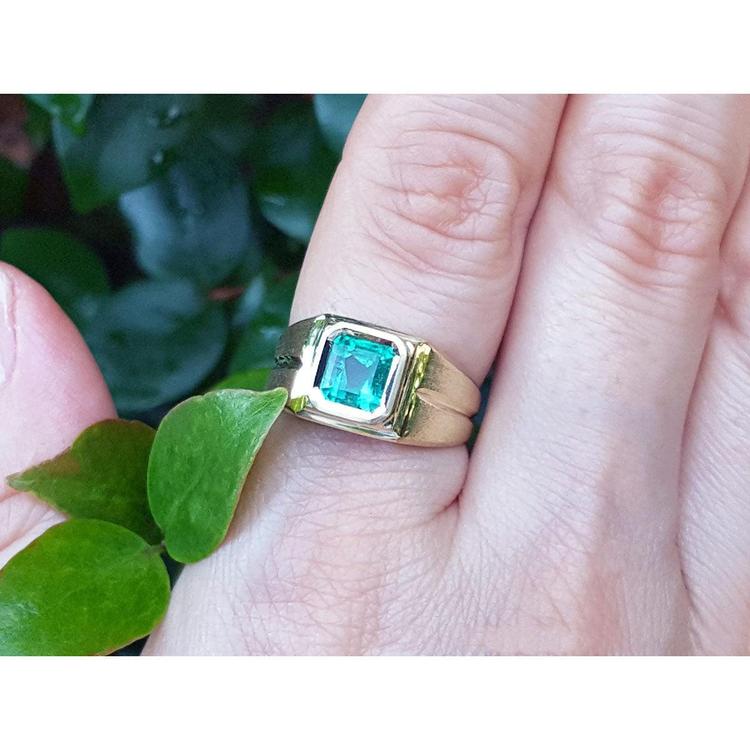 Gold pinky ring for men with a natural colombian emerald on a finger against a natural background.