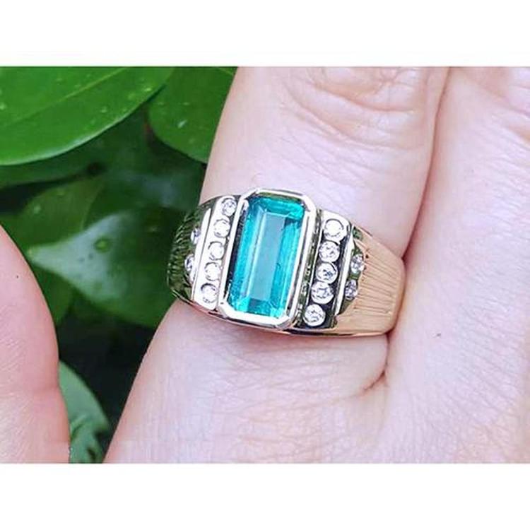 This men's emerald bezel set ring natural diamonds yellow 14k gold is on a finger against a green leafy background.