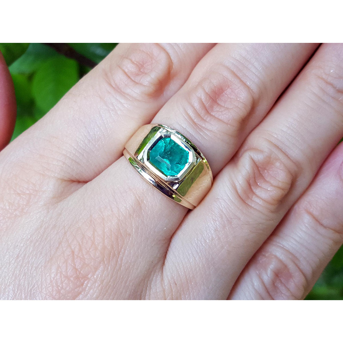 Gold ring with a bezel set genuine emerald on a hand against a blurred natural background.