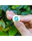 Gold horseshoe ring design with a colombian emerald held by a hand against a green leafy background.