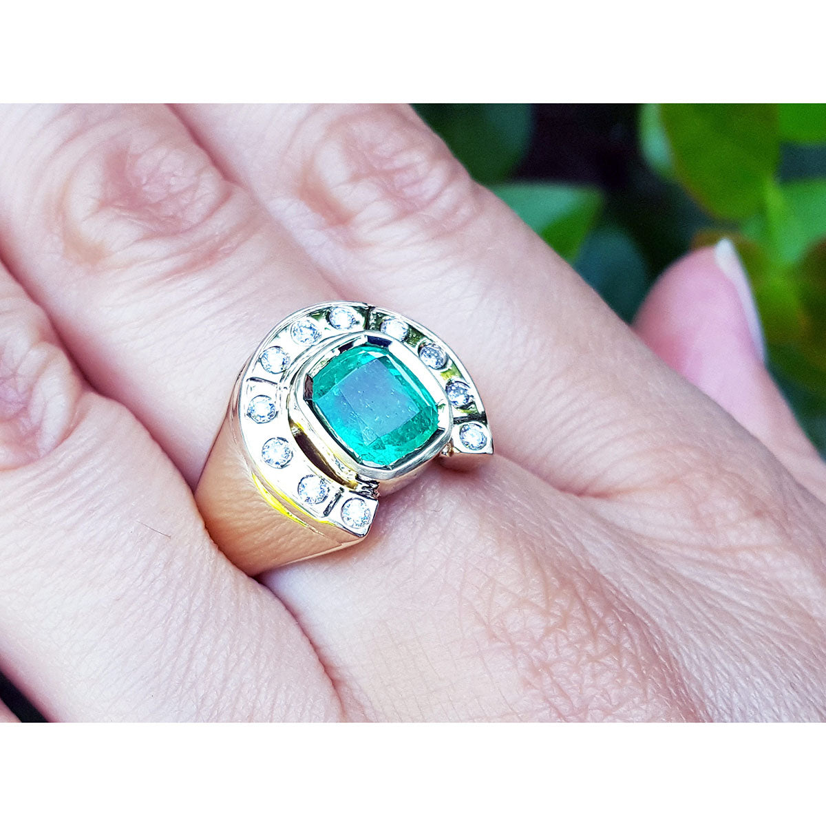 A men&#39;s emerald horseshoe ring with accent diamonds in yellow gold on a hand between fingers.