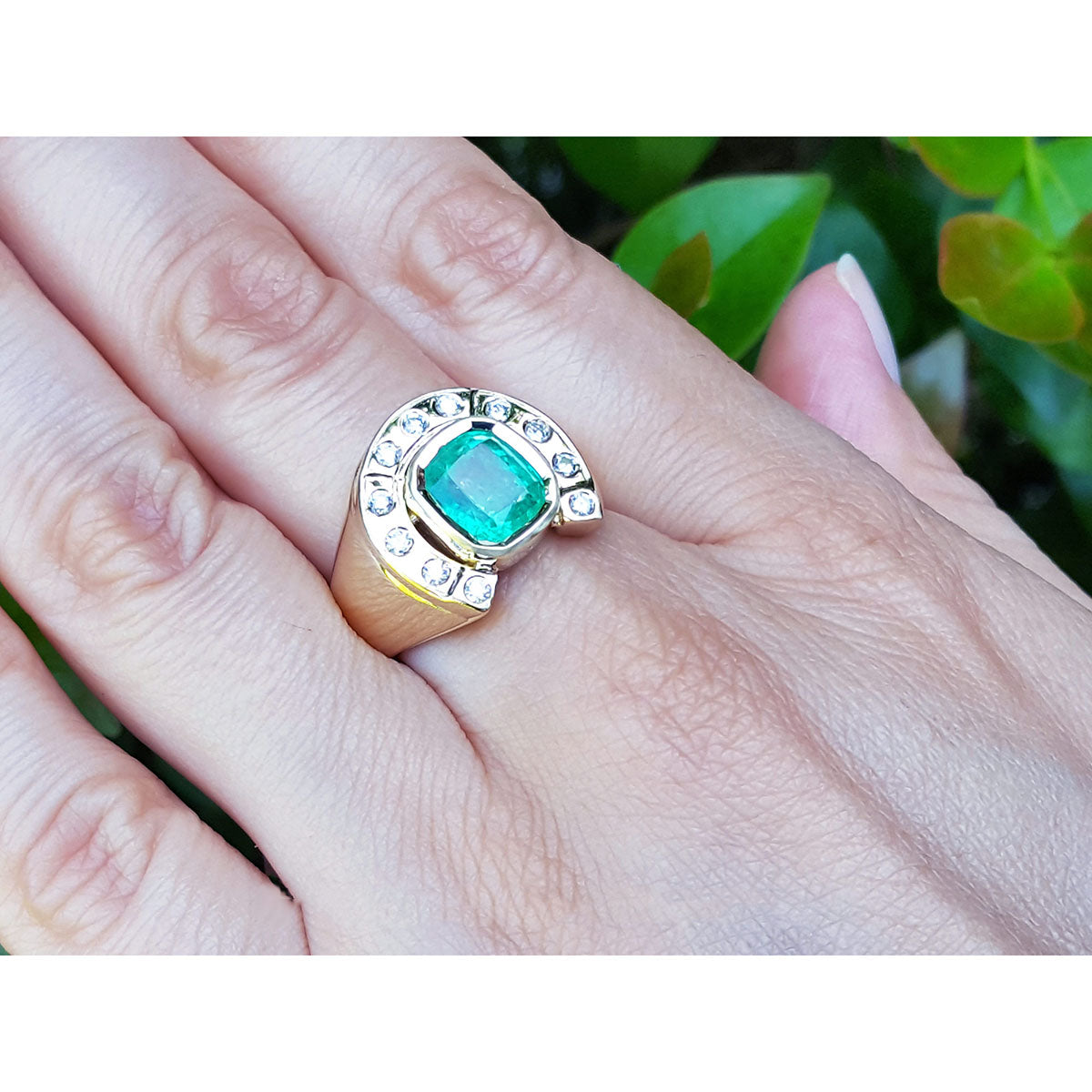 A yellow gold men&#39;s emerald ring horseshoe design on a hand against a blurred green background.