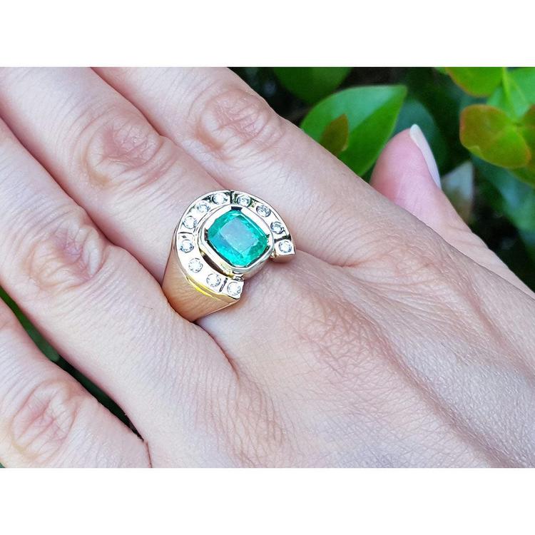 A yellow gold men's emerald ring horseshoe design on a hand against a blurred green background.