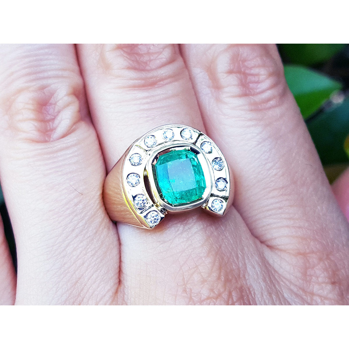 A gold men's emerald ring horseshoe design with accent diamonds on a hand.