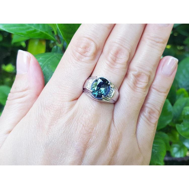 Men's 14K white gold ring with a deep greenish-blue oval sapphire and diamond accents on a hand.
