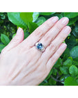 Hand wearing a men's natural Australian sapphire ring oval cut prong set 14K white gold, on leafy background