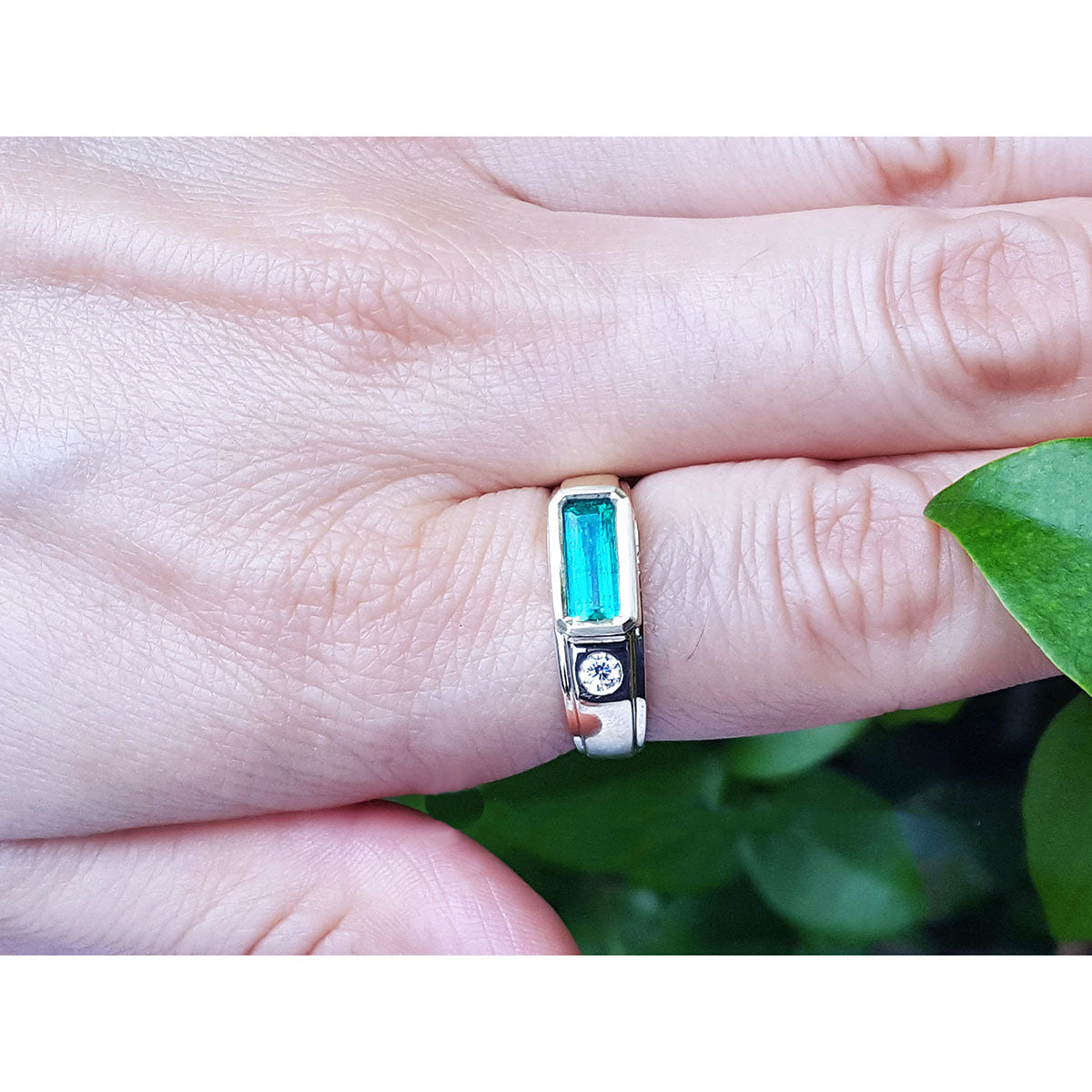 Ring with a genuine colombian emerald on a finger against a green leaf background.