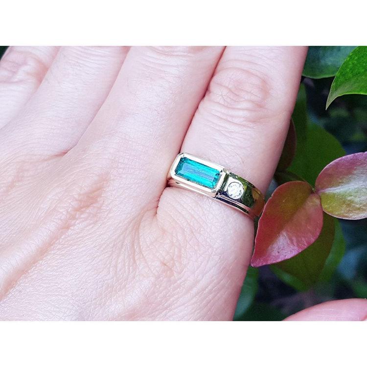 A 14k yellow gold men's emerald ring with accent single diamond on a person's hand.
