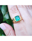 A yellow gold solitaire ring for men with a square emerald bezel set on a hand against a natural background.