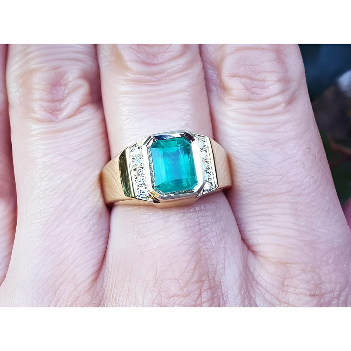 
This 18k yellow gold men's emerald ring is in bezel set and has accent natural diamonds on a person's finger.