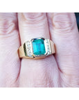 
This 18k yellow gold men's emerald ring is in bezel set and has accent natural diamonds on a person's finger.