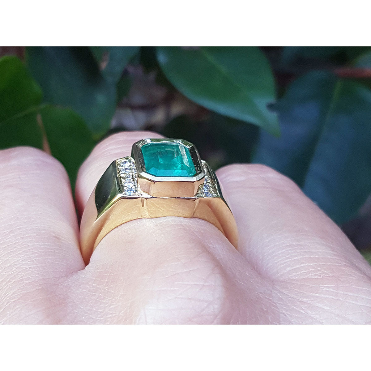 Gold ring for men with accent natural diamond on a finger against a leafy background.